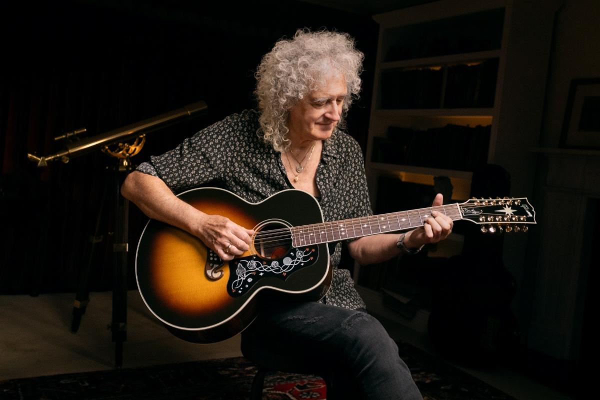 Brian May plays a Gibson twelve-string acoustic guitar while seated