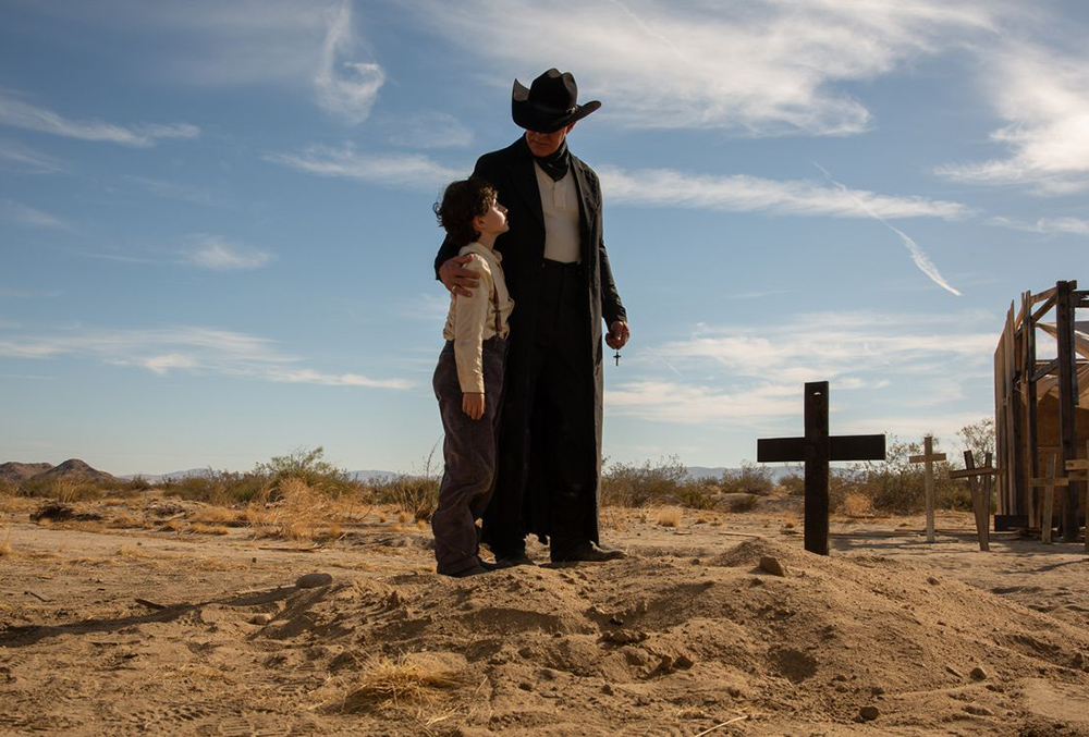Western film scene with a cowboy standing near a wooden cross in the desert