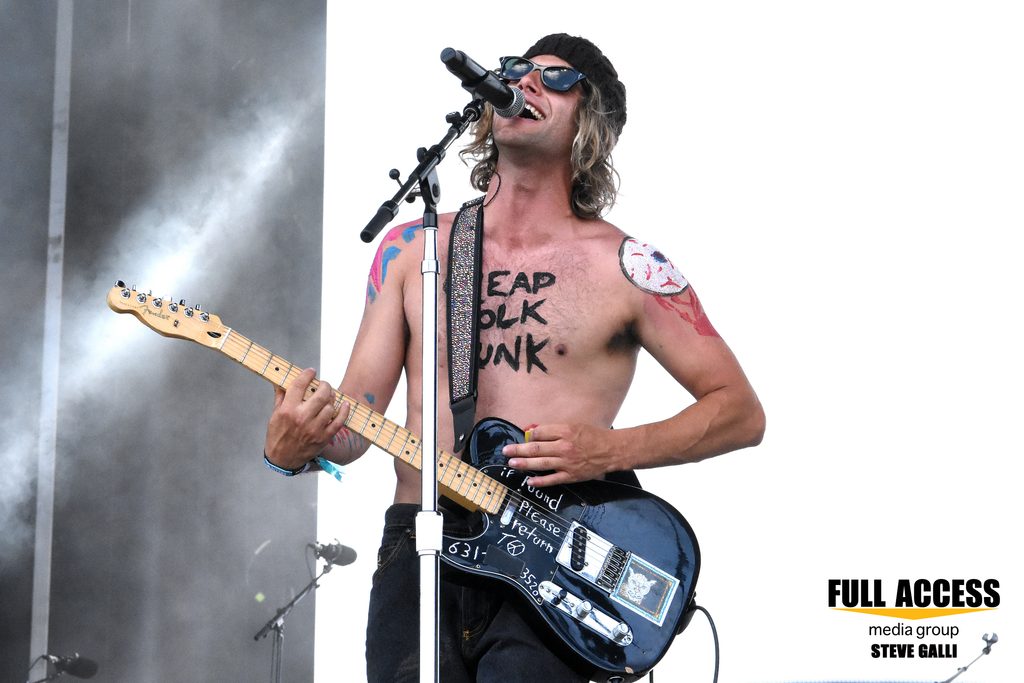 Shirtless guitarist singing into a microphone at Bonnaroo