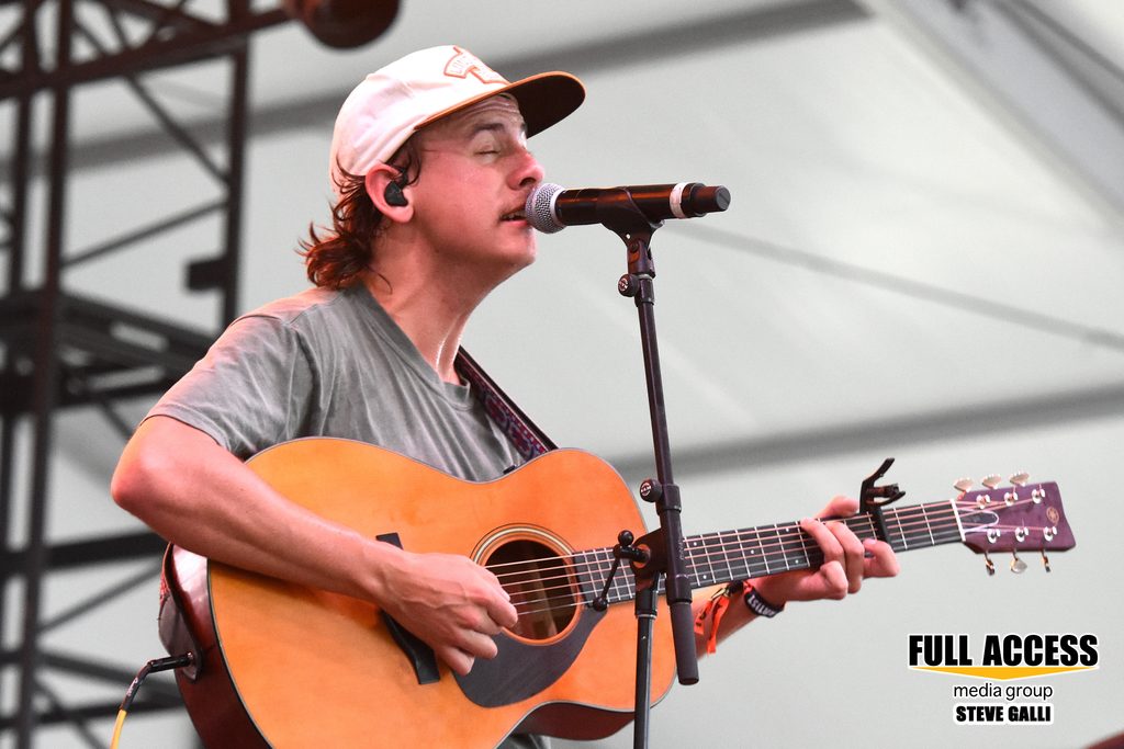 Singer in a baseball cap playing an acoustic guitar at Bonnaroo