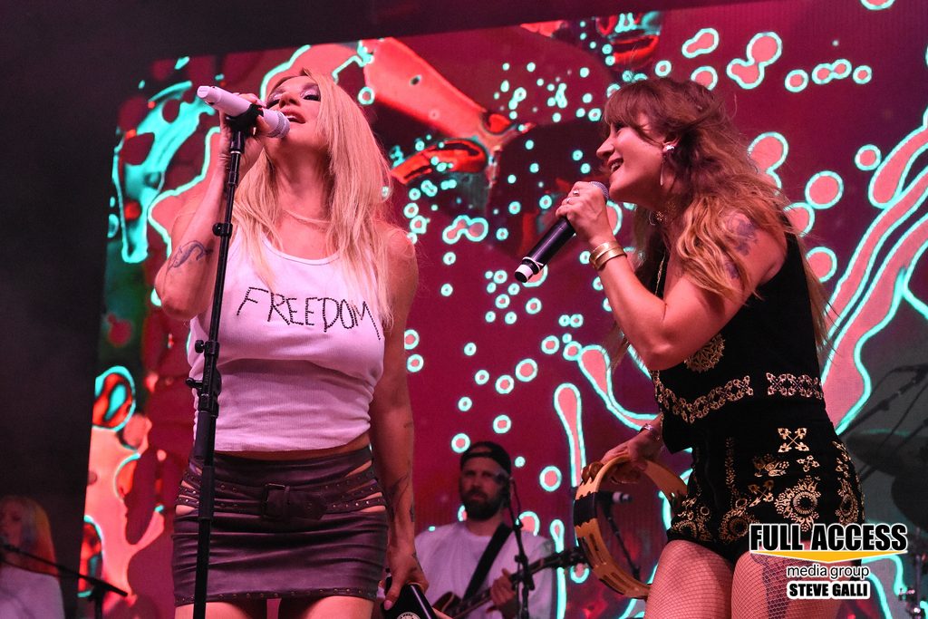 Two vocalists singing together in front of a colorful festival screen