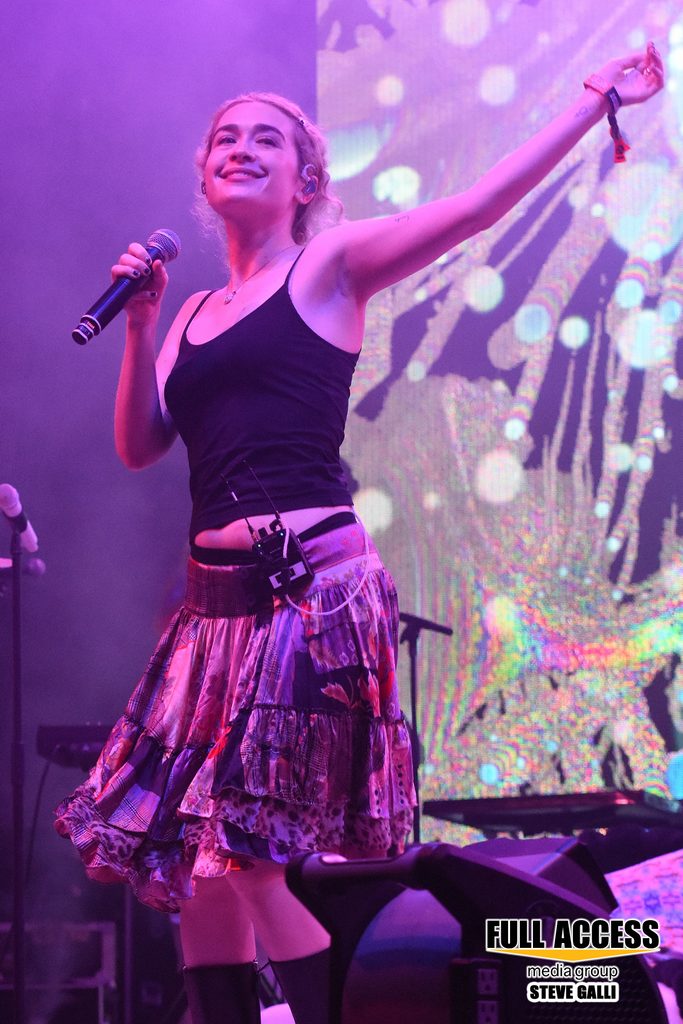 Singer in a plaid skirt raising an arm toward the festival crowd