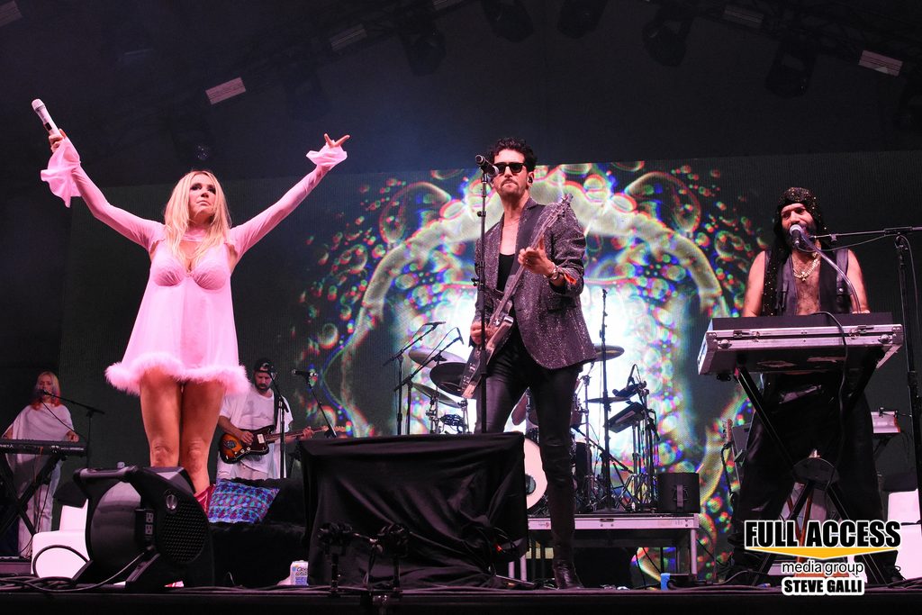 Singer in a pink dress raising both arms beside guest musicians