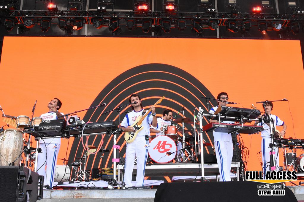 Band in white outfits performing in front of an orange stage backdrop