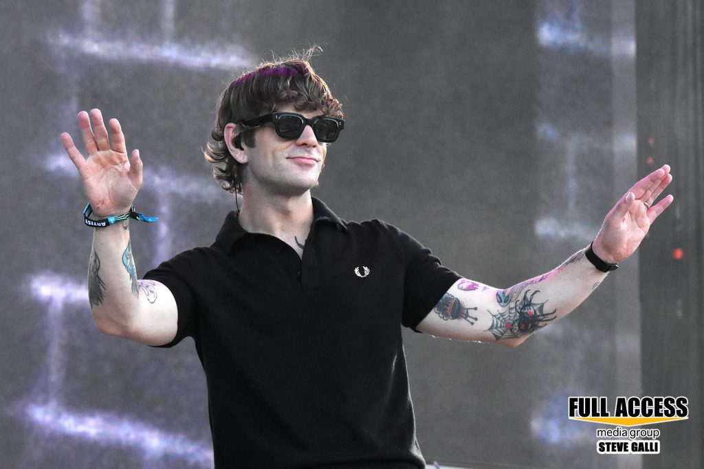 Vocalist in sunglasses raising both hands toward the festival crowd