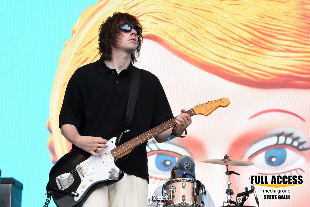 Guitarist in sunglasses playing in front of a colorful face illustration