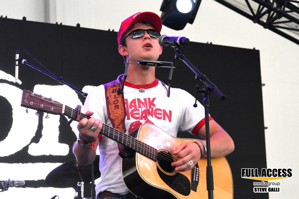 Musician in a red cap singing with an acoustic guitar and harmonica