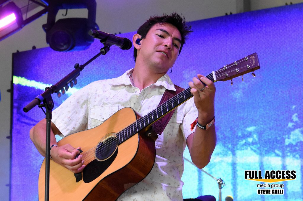 Musician playing an acoustic guitar under purple festival lighting
