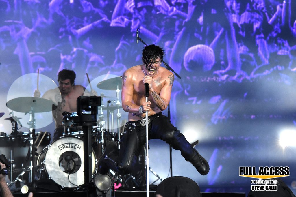 Shirtless vocalist jumping beside the drum kit during a festival performance