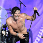 Shirtless vocalist leaning toward the audience with a microphone at Bonnaroo