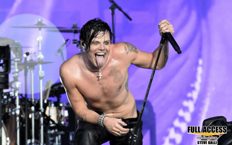 Shirtless vocalist leaning toward the audience with a microphone at Bonnaroo