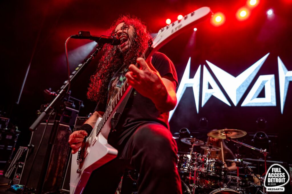 Guitarist singing in front of the Havok backdrop under red lights