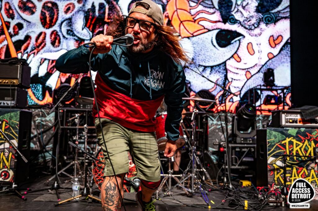 Vocalist in a backward cap performing in front of illustrated stage artwork