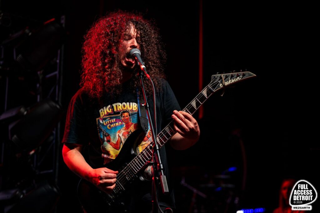 Curly-haired guitarist singing into a microphone during the Fillmore show