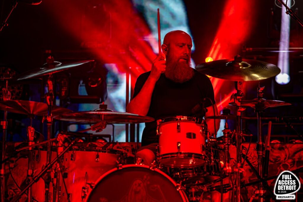 Drummer playing a red drum kit beneath red stage beams