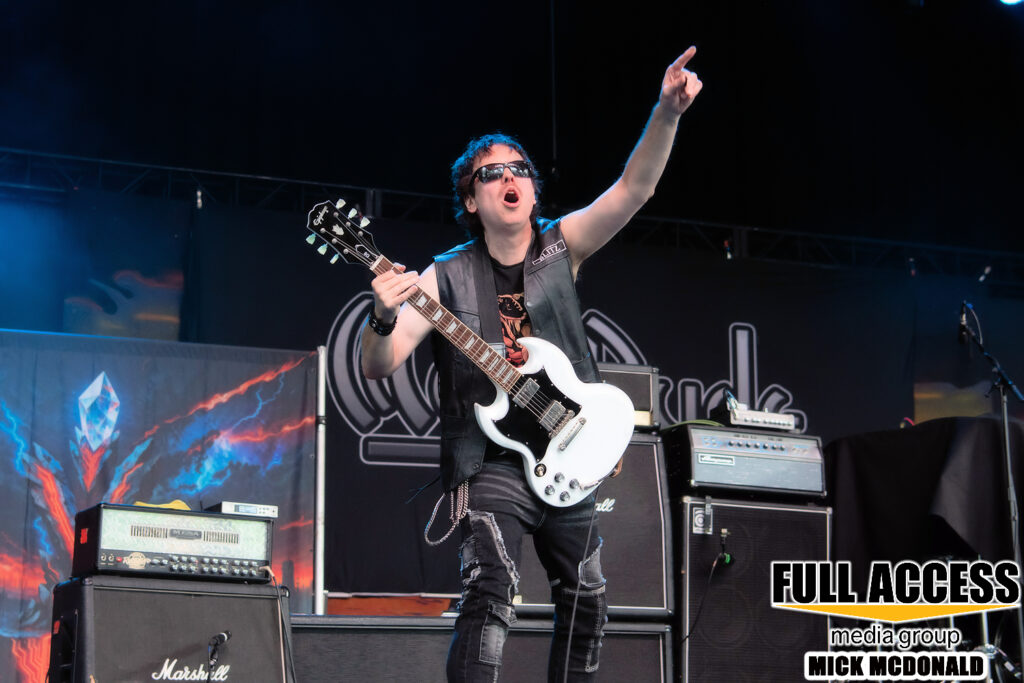 Bassist pointing upward while holding a white electric bass