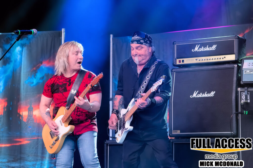 Two guitarists playing beside Marshall amplifiers under blue lights