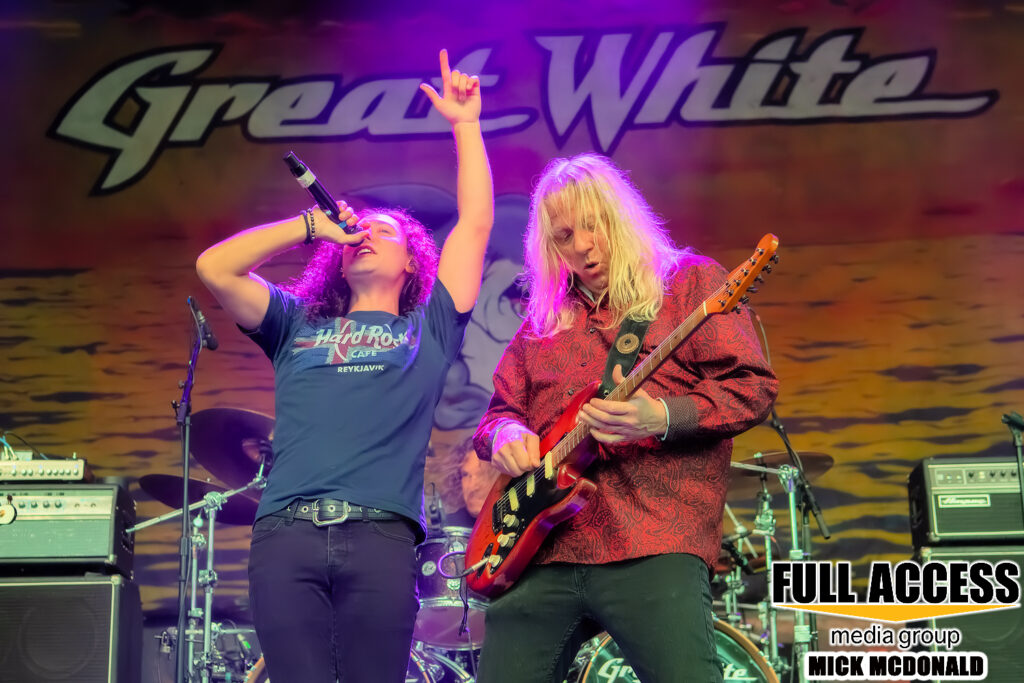 Singer and guitarist performing in front of the Great White backdrop
