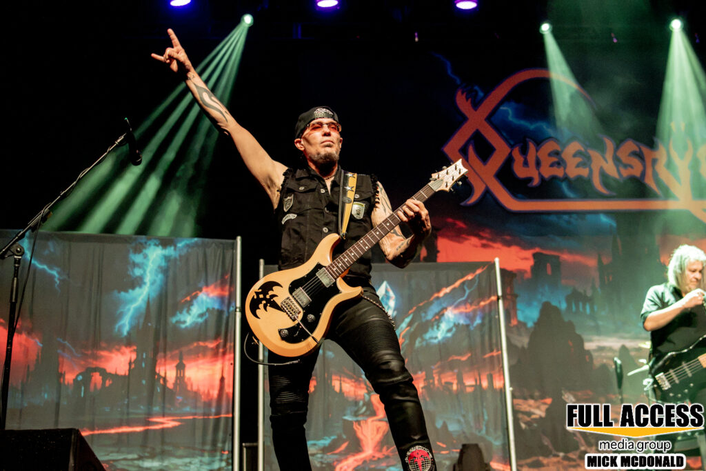 Guitarist raising an arm in front of the Queensrÿche backdrop