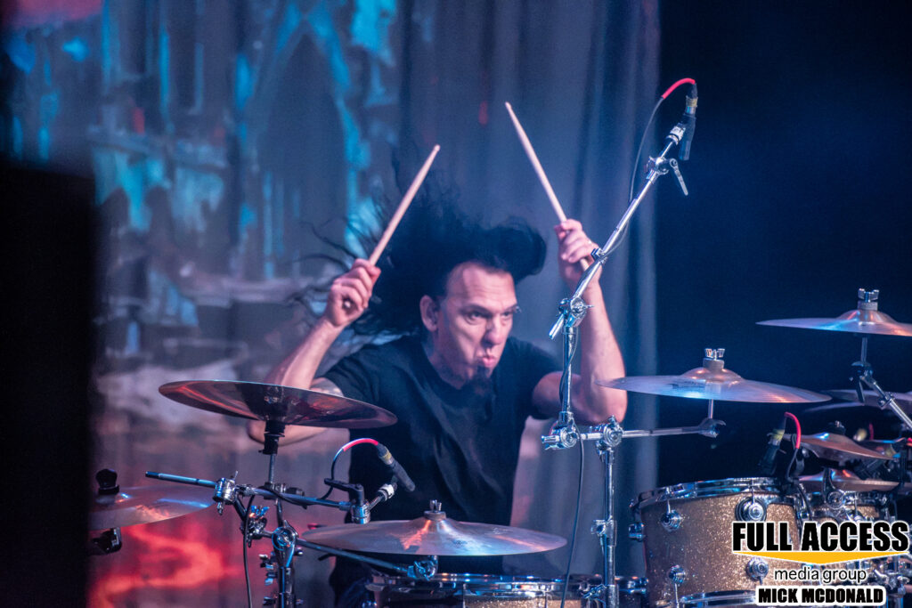 Drummer raising both drumsticks above the kit during a concert