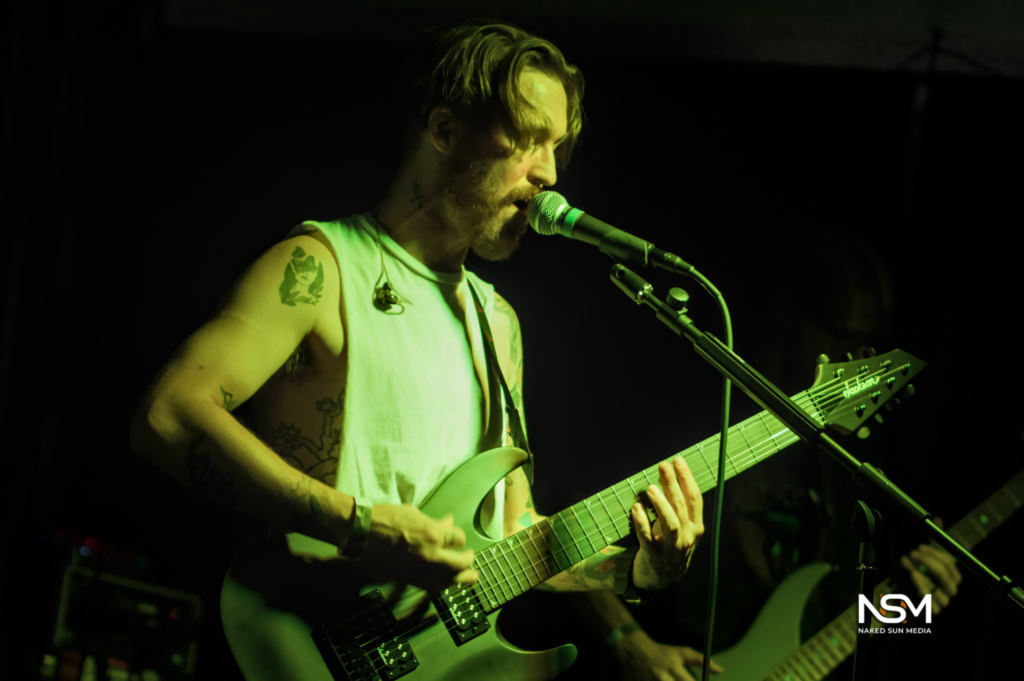 Guitarist singing into a microphone under green stage lighting