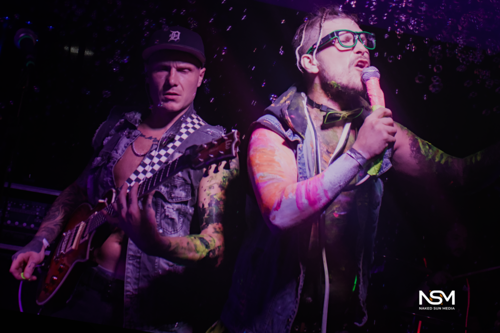 Vocalist and guitarist performing under purple stage lighting