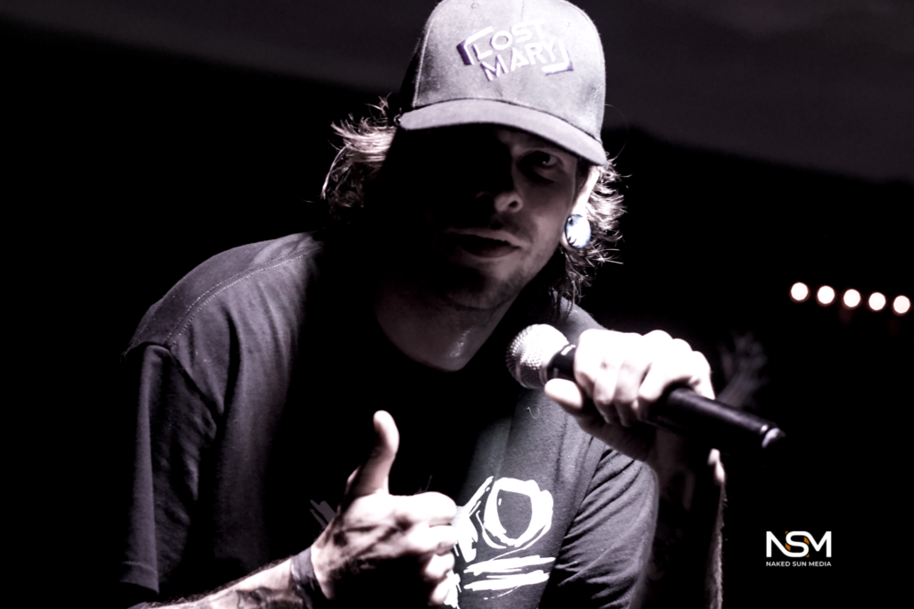 Black-and-white concert photograph of a vocalist wearing a cap