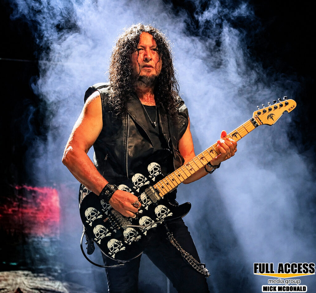 Guitarist playing a patterned electric guitar amid stage fog