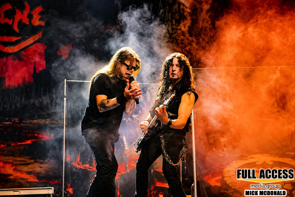 Vocalist and guitarist performing amid orange-lit stage fog