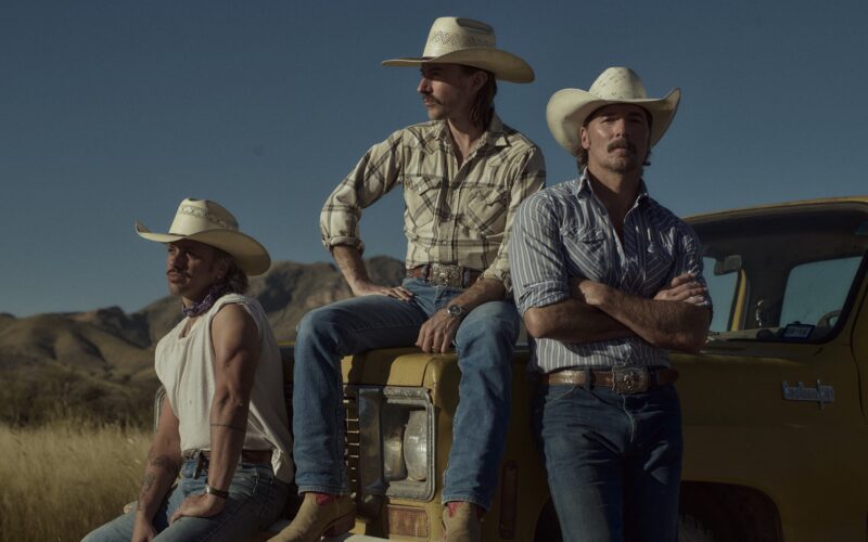 Midland band members in cowboy hats beside a yellow vehicle in the desert.