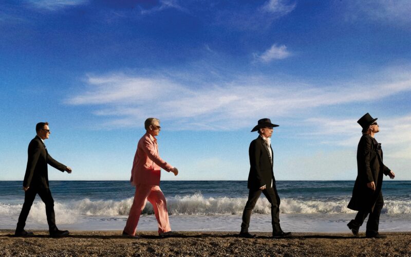 U2 band members walking together on a beach.